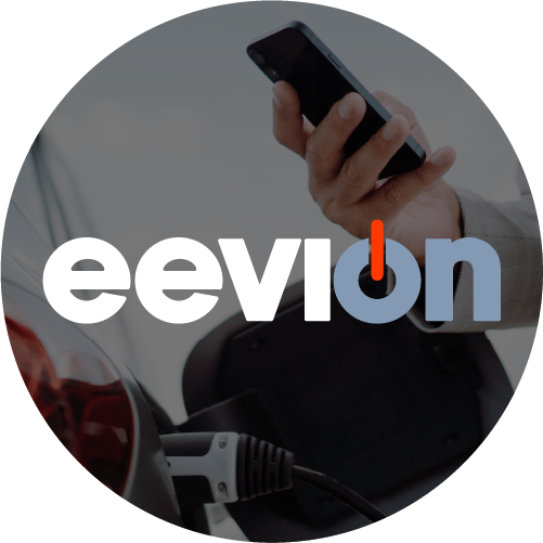 A hand holds a smartphone above a charging electric vehicle. The word eevion is overlaid, with the i resembling a power button.